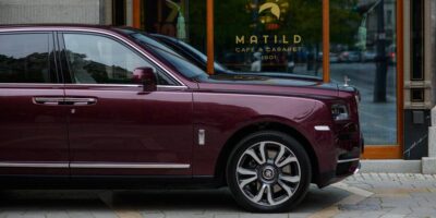 The 2025 Rolls-Royce Cullinan parked beside a stylish café, highlighting its sleek design, chrome accents, and the intricate detailing of its alloy wheels.