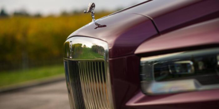 A close-up view of the Spirit of Ecstasy hood ornament on the grille of the 2025 Rolls-Royce Cullinan, showcasing its signature luxurious design against a blurred green landscape background.