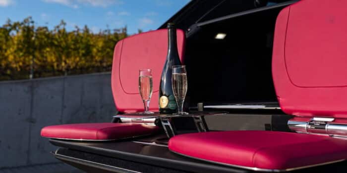 Close-up of the 2025 Rolls-Royce Cullinan's bespoke tailgate setup with vibrant red seating and a champagne bottle, exemplifying opulence and practicality.