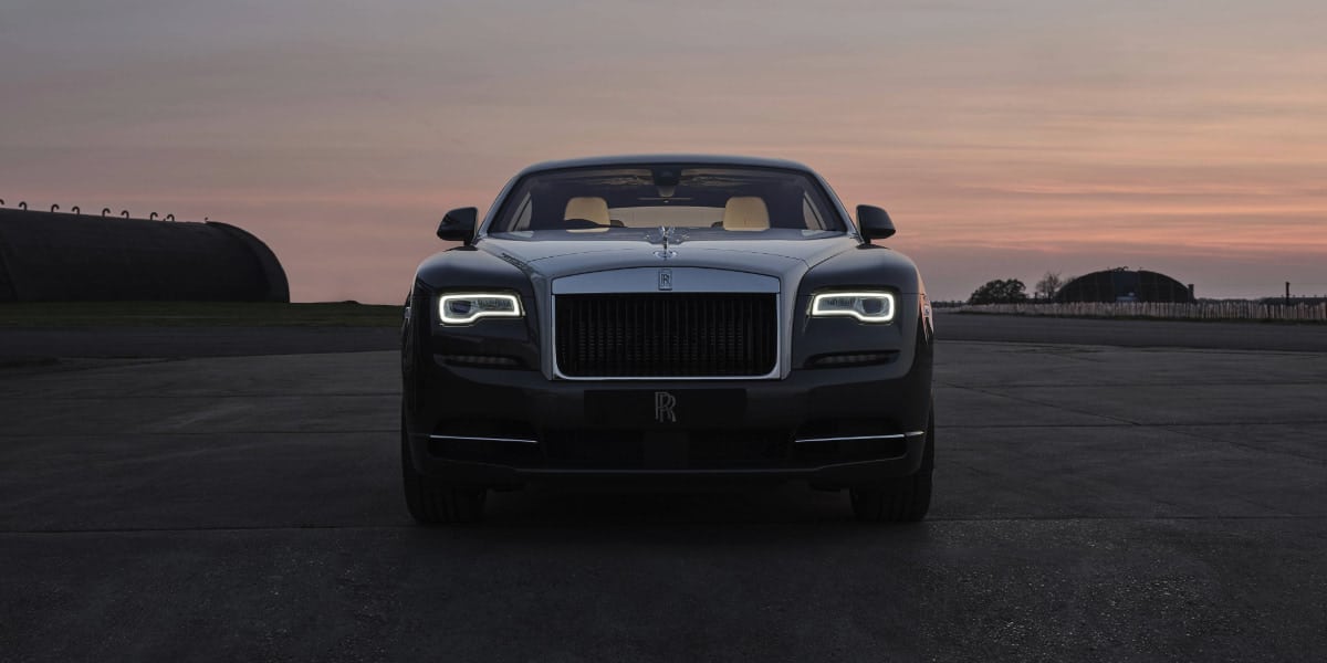 A front-facing view of a Rolls-Royce Wraith at dusk, showcasing its illuminated headlights and luxury design. The Rolls-Royce Wraith interior offers premium comfort and bespoke craftsmanship.