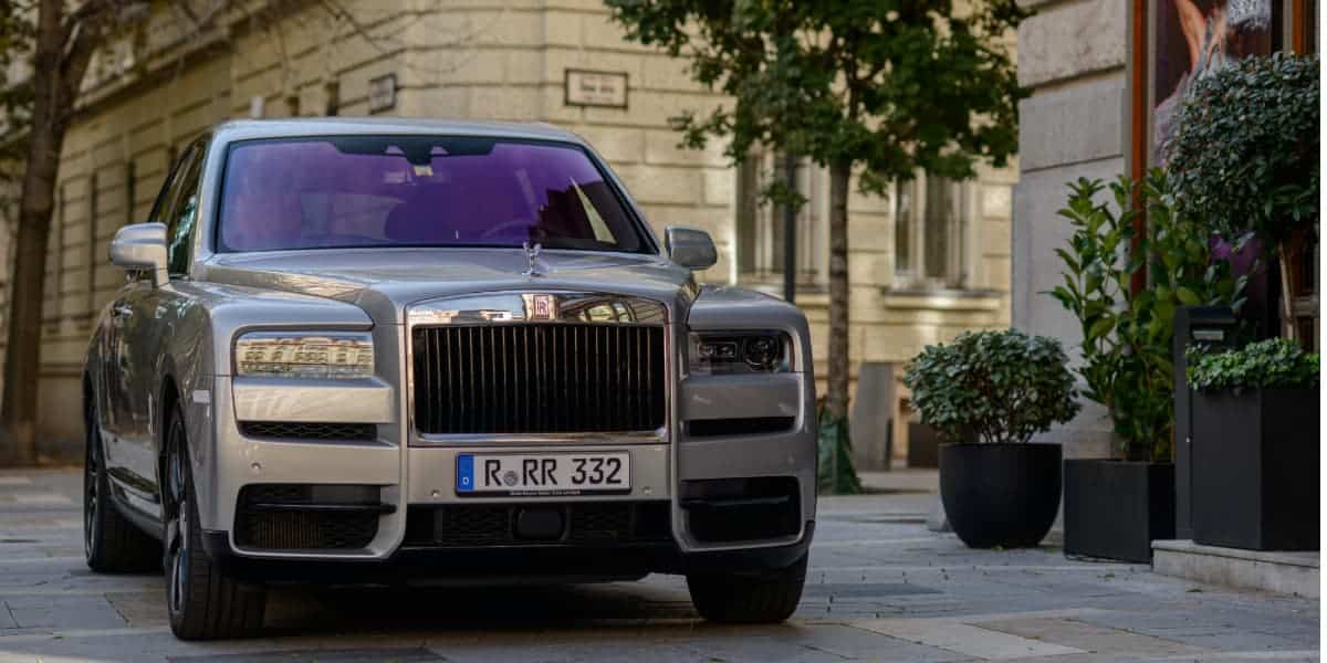 Front view of a silver rolls-royce cullinan luxury SUV parked on a city street with trees and buildings in the background.
